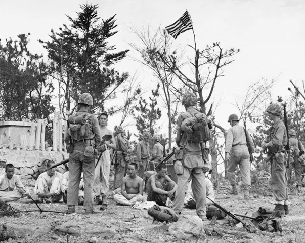 3/5 Marines raise the American flag on Wolmi-do, while North Korean prisoners are guarded by onlooking Marines.